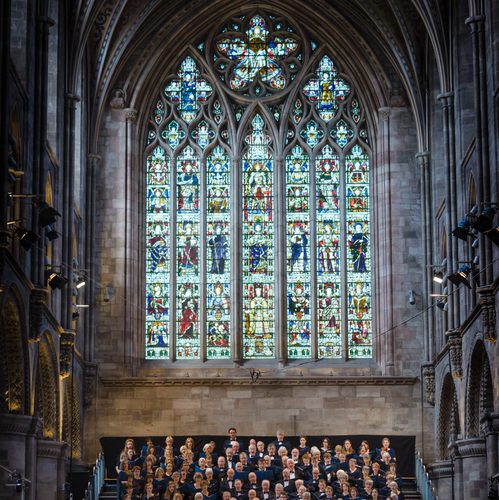 Festival chorus in front of Hereford Cathedral stain glass window