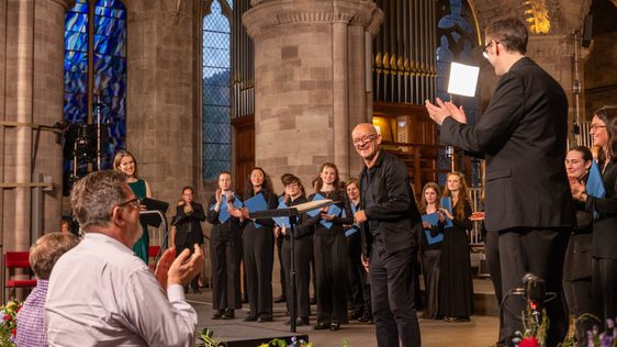 Composer Bob Chilcott receiving applause on stage for his piece of music.