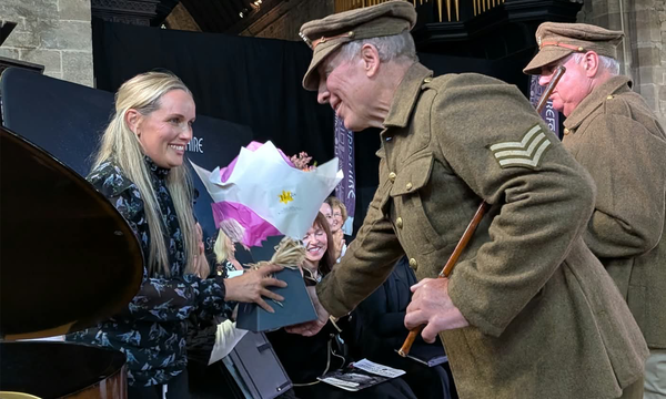 Soldier shakes hands with conductor holding a bouquet of flowers