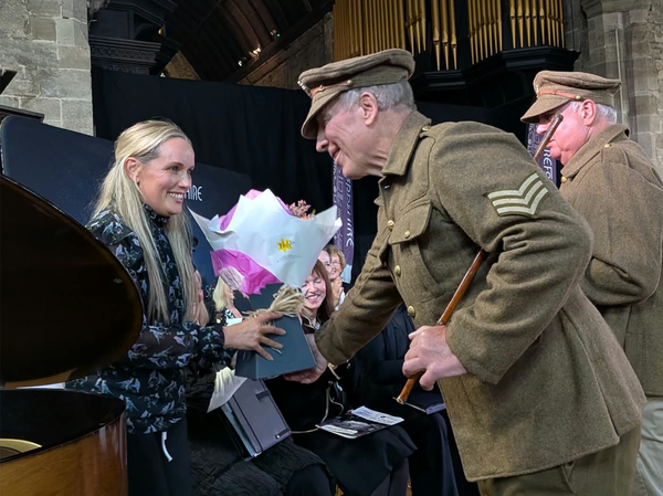 Soldier shakes hands with conductor holding a bouquet of flowers